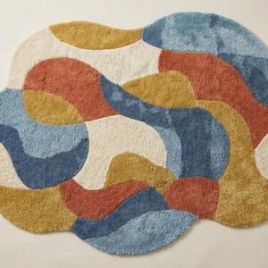 May include: A colorful, abstract rug with a cloud-like shape. The rug features a mix of colors, including blue, orange, yellow, and cream. The rug is made of a soft, textured material, and would be a great addition to any room.