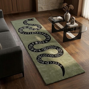 May include: A rectangular runner rug in a muted sage green colour featuring a large, winding black snake graphic. The snake's body is decorated with white geometric patterns and runic-style symbols that span the entire length of the floor covering.