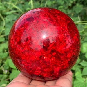 Könnte beinhalten: Ein kugelförmiges Objekt aus durchscheinendem rotem Glas mit einer rissigen Innenstruktur. Die Oberfläche ist glatt und poliert, reflektiert das Licht auf der runden Form und zeigt tiefe karmesinrote Farbtöne sowie komplexe Muster.