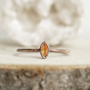 May include: A delicate copper ring with a marquise-shaped orange gemstone.