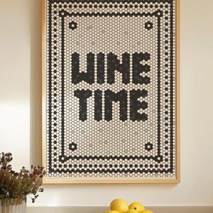May include: A framed artwork with the words "WINE TIME" in black block letters. The artwork is made of small, hexagonal tiles in shades of black, white, and gray, set within a wooden frame. A bowl of lemons sits below.