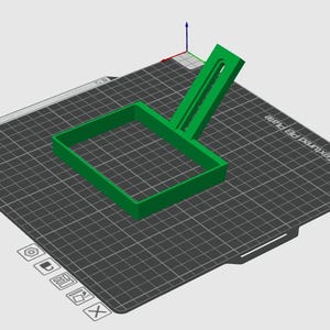 Può includere: Un oggetto verde brillante stampato in 3D, possibilmente uno strumento o un componente, con un telaio rettangolare e un'impugnatura attaccata. L'oggetto è posizionato su una superficie grigio scuro, strutturata, con un motivo a griglia. La superficie presenta il testo "Bambu Textured PE Plate".