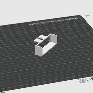 May include: A 3D-rendered, white rectangular object with a smaller rectangular piece attached, positioned on a black grid. The object is likely a component or part of a larger design. The background is a light gray color.