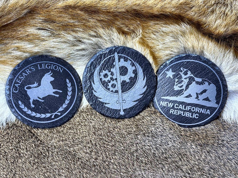 May include: Three round, black slate coasters with etched designs. One features a bull and the text "CAESAR'S LEGION", another has a gear and wing design, and the third displays a bear and the text "NEW CALIFORNIA REPUBLIC".