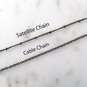 Photo reference of the chain styles available, which include a satellite chain that has ball accents and a traditional cable chain that has small circular links. Both chains are antique brass plated.