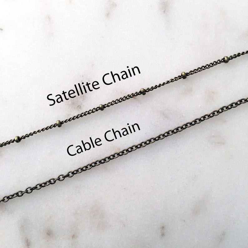 Photo reference of the chain styles available, which include a satellite chain that has ball accents and a traditional cable chain that has small circular links. Both chains are antique brass plated.