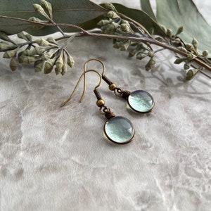 An angled side view of the spring raindrop earrings showcasing the translucent nature of the light green glass in the light.