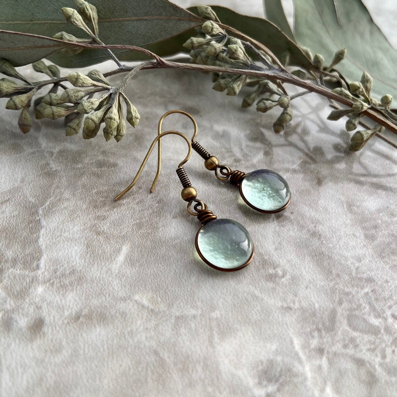 An angled side view of the spring raindrop earrings showcasing the translucent nature of the light green glass in the light.