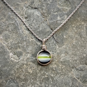 May include: A silver chain necklace with a small round pendant. The pendant is made of glass and has a black, white, and green striped design.