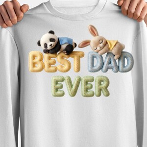 May include: White sweatshirt with the text "BEST DAD EVER" in yellow, blue, and green. A panda and a bunny are resting on the letters. The panda wears a blue blanket, and the bunny wears a yellow blanket.