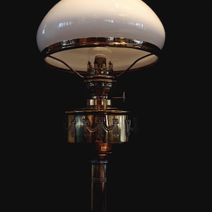 May include: An antique oil lamp with a white glass shade and brass base. The lamp features intricate detailing on the brass components, including the base and the oil reservoir. The lamp is designed with a classic, vintage aesthetic.