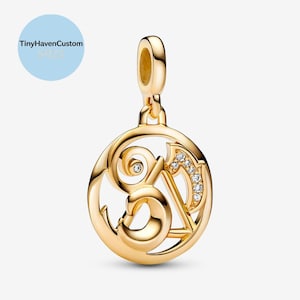 May include: A gold-colored pendant with a circular design. The pendant features an ornate letter "S" and "A" with embedded clear crystals. The pendant has a loop at the top for attaching to a chain. The text "TinyHavenCustom S925" is in a light blue circle.