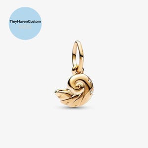 Pode incluir: Um berloque dourado em forma de concha de nautilus, com uma argola para prender a uma pulseira ou colar. O berloque tem um design em espiral e pequenos detalhes em forma de estrela. O texto "TinyHavenCustom S925" está em um círculo azul claro.