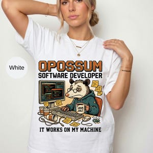 May include: A white t-shirt featuring a graphic of an opossum wearing glasses and a teal hoodie, sitting at a computer desk. The text reads OPOSSUM SOFTWARE DEVELOPER and IT WORKS ON MY MACHINE. The graphic includes a monitor, keyboard, and mug.