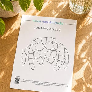Op de afbeelding: Een wit papier met een zwarte lijntekening van een springspin. De tekst "Forest Aura Art Studio" en "JUMPING SPIDER" zijn boven de spin gedrukt. Het Etsy shop logo en tekst staan linksonder.