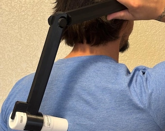 May include: A black, articulated, L-shaped plastic applicator tool with a circular holder at one end, currently gripping a white cylindrical bottle against a blue t-shirt. The device features a central hinge with a visible adjustment knob.