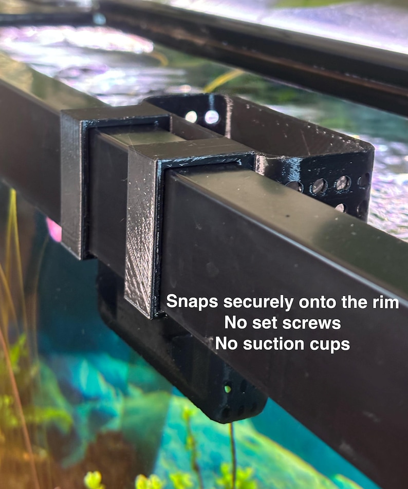 May include: Black plastic aquarium rim clip. The clip has a rectangular shape with a curved section and several small holes. Text on the image reads "Snaps securely onto the rim. No set screws. No suction cups."
