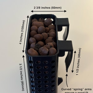 May include: Black rectangular plant pot with curved spring arms. The pot is 4 inches (100mm) tall, 3 1/2 inches (90mm) wide, and 1 5/8 inches (40mm) deep. It is filled with brown pebbles. The text "Frameless" is at the top.
