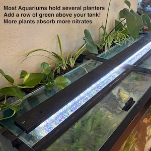May include: An aquarium with a row of green plants above the tank. The plants are in a black planter with a bright LED light. The text on the wall says, "Most Aquariums hold several planters. Add a row of green above your tank! More plants absorb more nitrates."