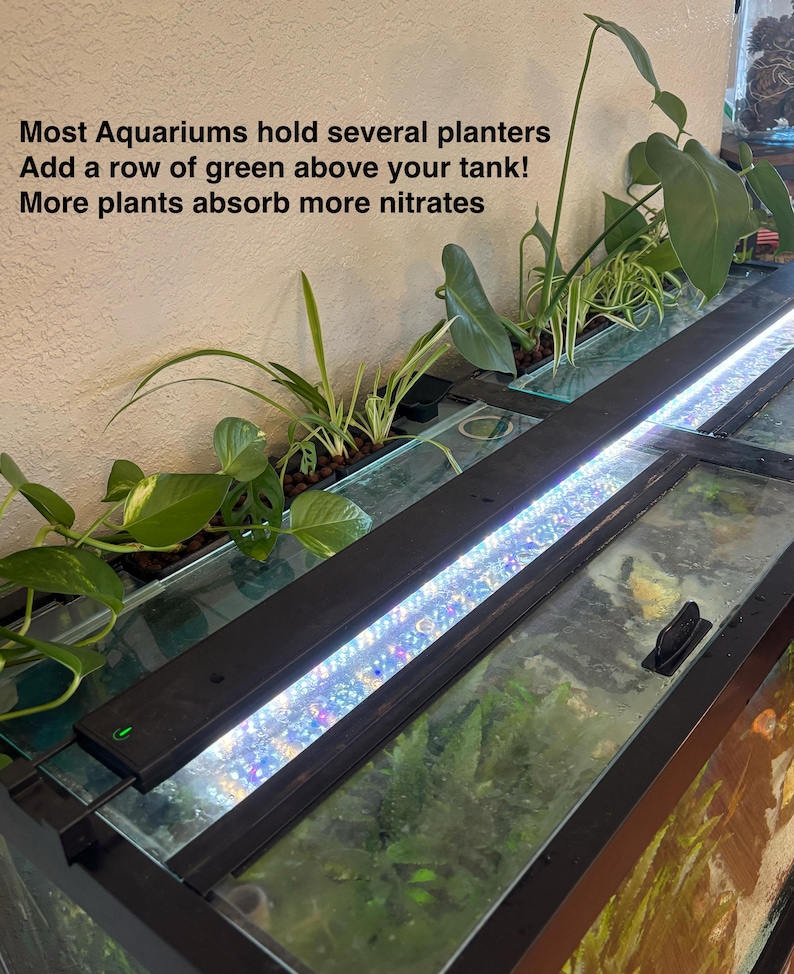 May include: An aquarium with a row of green plants above the tank. The plants are in a black planter with a bright LED light. The text on the wall says, "Most Aquariums hold several planters. Add a row of green above your tank! More plants absorb more nitrates."