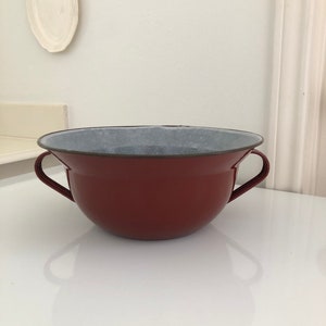 May include: A red enamel bowl with two handles. The bowl has a white interior.