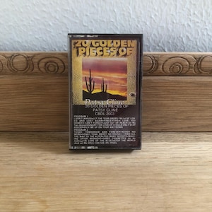 May include: A cassette tape with a sunset desert scene on the cover. The title is "20 Golden Pieces of Patsy Cline". The cassette tape is a compilation of 20 songs by the country music singer Patsy Cline.