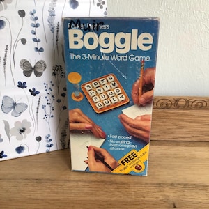 May include: A blue box for the Boggle board game. The box features a picture of the game board with letter tiles and a timer. The text on the box reads "Boggle The 3-Minute Word Game".