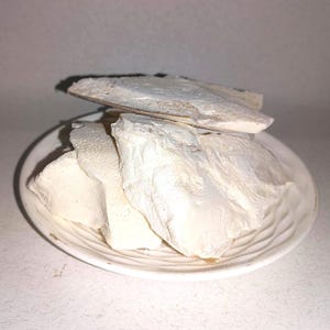 May include: A white ceramic plate holds several pieces of white, irregularly shaped food. The food appears to be layered and has a slightly rough texture. The plate has a simple, ridged design.