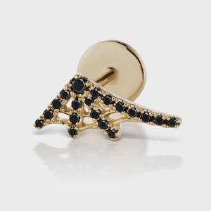 Op de afbeelding: Een goudkleurige oorbel met een geometrisch ontwerp. De oorbel heeft een driehoekige vorm met zwarte edelstenen. De pin en de achterkant zijn ook goudkleurig. De oorbel is ontworpen voor een enkele oor piercing.