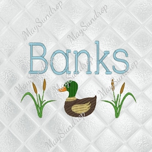 Può includere: Design ricamato con il nome "Banks" in azzurro, sopra un'anatra e delle tife. L'anatra ha la testa verde, il corpo marrone e il becco arancione. Lo sfondo è un motivo trapuntato bianco.