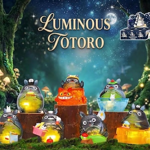 May include: A collection of luminous Totoro figurines in various poses, illuminated from within. The figurines are set against a whimsical forest backdrop with mushrooms and a starry night sky. The text "Luminous Totoro" is displayed at the top.