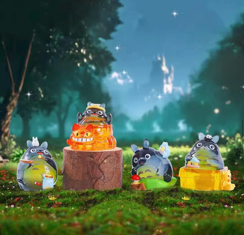 May include: A collection of translucent figurines of the character Totoro from the animated film My Neighbor Totoro. The figurines are in various poses and colors, set against a forest backdrop with a wooden stump.
