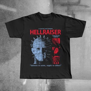 May include: Black t-shirt featuring the movie title "HELLRAISER" in red and the film's name. The design includes a blue and white image of a character with pins and the quote "demons to some, angels to others."