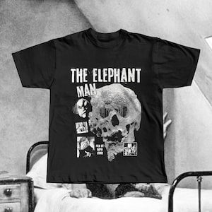 May include: Black t-shirt featuring the movie title "The Elephant Man" in white block letters above a detailed skull graphic. The shirt also includes the text "Film by David Lynch" and several small image stills.