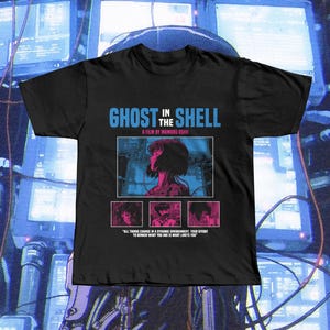 May include: Black t-shirt featuring the text "GHOST IN THE SHELL" in blue and white, with a film still graphic. Below the graphic are three smaller images and a quote. The shirt is a crew neck.