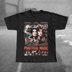Puede incluir: Camiseta negra con un diseño de cartel de película de "Practical Magic". El diseño incluye retratos de Sandra Bullock y Nicole Kidman, junto con el título de la película en rojo. La camiseta también enumera al director y al autor.