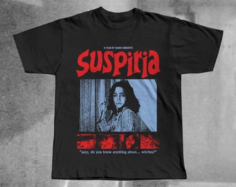 Puede incluir: Una camiseta negra de manga corta con el texto rojo SUSPIRIA, un gráfico azulado de una persona y cuatro imágenes más pequeñas con tonos rojos. Debajo de los gráficos, el texto dice: A FILM BY DARIO ARGENTO y "Suzy, do you know anything about... witches?"