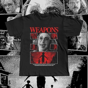 Puede incluir: Camiseta negra con la palabra "WEAPONS" en rojo. La camiseta presenta un gráfico de un hombre con gafas y varias imágenes más pequeñas del mismo hombre. Debajo, un gráfico rojo de niños y texto.
