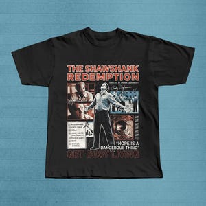 May include: Black t-shirt with a graphic design from the film "The Shawshank Redemption." The design includes film stills, the title, director's name, and the quote "Hope is a dangerous thing." The words "Get Busy Living" are also included.