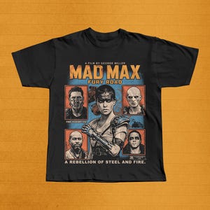 May include: Black t-shirt featuring the movie poster for "Mad Max: Fury Road." The design includes the film's title, character portraits, and the text "A Rebellion of Steel and Fire." The poster is in shades of orange, blue, and brown.