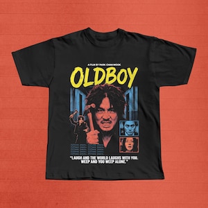 Könnte beinhalten: Schwarzes T-Shirt mit dem Filmtitel "OLDBOY" in Gelb und einer Grafik eines Mannes mit einem Hammer. Das Shirt enthält auch den Text "A FILM BY PARK CHAN-WOOK" und das Zitat: "LAUGH AND THE WORLD LAUGHS WITH YOU. WEEP AND YOU WEEP ALONE."