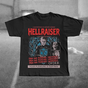 Puede incluir: Camiseta negra con el título de la película "HELLRAISER" en rojo, y un gráfico de un personaje. La camiseta también presenta el texto "A MASTERPIECE OF MODERN HORROR", "A FILM BY CLIVE BARKER", y la cita "YOUR PLEASURE IS OUR PAIN."