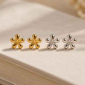 May include: Four stud earrings shaped like five-petaled flowers. Two earrings are finished in a polished gold tone, and two earrings are finished in a polished silver tone. Each earring features rounded, smooth petals radiating from a central point.