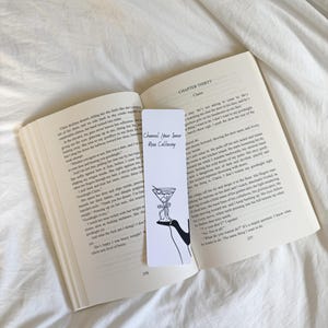 May include: A white ceramic mug with a black handle and the text "But First, Coffee" in a bold, black font. The mug is set against a blurred background, suggesting a cozy setting.