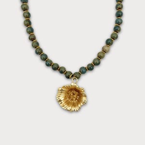 May include: A necklace with dark green and gold beads, and a gold-coloured flower pendant. The beads are connected with gold-coloured accents. The necklace is a piece of jewellery.