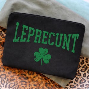 Può includere: Pochette nera con cerniera con la scritta "LEPRECONT" in lettere verdi consumate e un trifoglio verde. La pochette è rettangolare e poggia su una superficie con stampa leopardata.