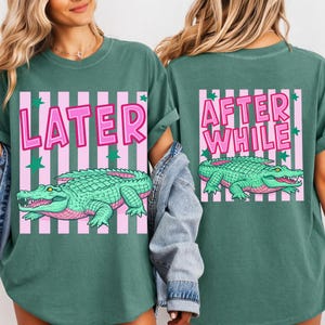 May include: Green t-shirts with a pink and white striped design. The front of the shirt says "LATER" with a green alligator graphic. The back of the shirt says "AFTER WHILE" with a matching alligator graphic.
