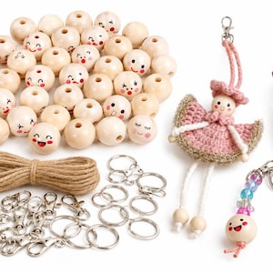 May include: A craft kit containing numerous light-colored wooden beads with painted facial expressions, a coil of brown jute twine, several silver-toned metal lobster clasps and key rings, a crocheted doll charm, a mushroom charm, and a beaded keychain.