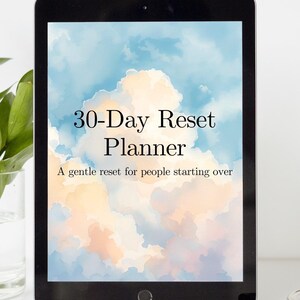 Pode incluir: Um tablet preto exibe um planejador digital com o texto "30-Day Reset Planner" e "A gentle reset for people starting over". O fundo apresenta um design de nuvens pastel em tons de azul, pêssego e branco.