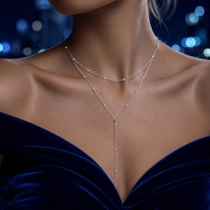 May include: A delicate silver-toned layered necklace featuring two thin chains adorned with small, evenly spaced round clear stones. The upper chain forms a choker style, while the lower chain extends into a vertical drop, creating a Y-shaped design.